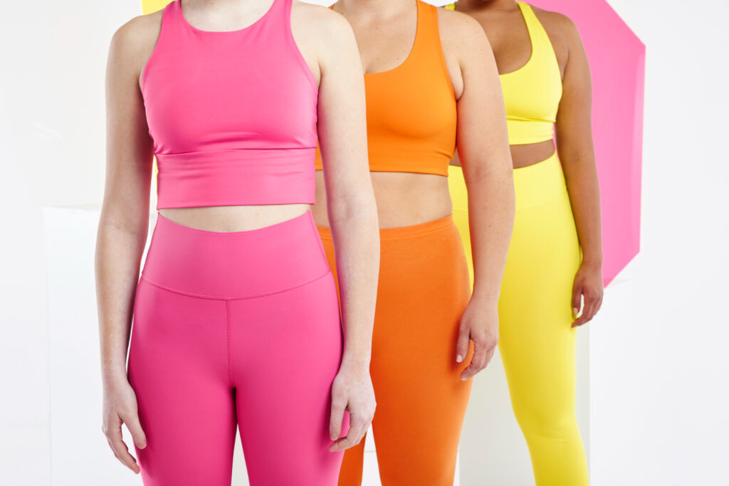Des tenues de fitness pour femme (haut et bas) de couleur rose, orange et jaune.