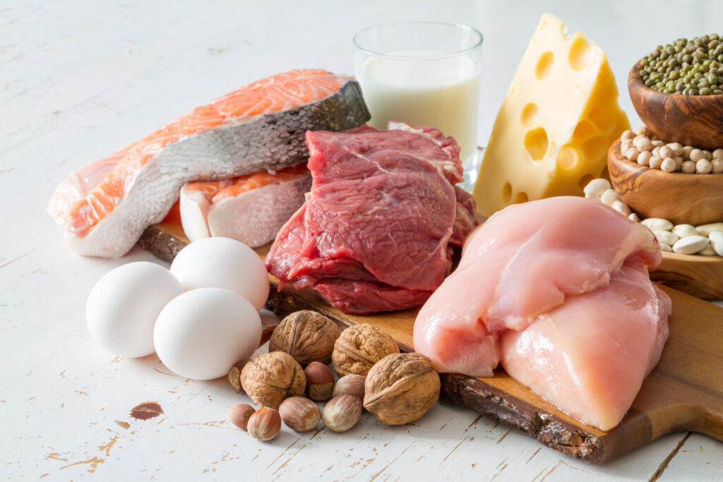 Différents aliments sources de protéine: viande de boeuf, viande de poulet, poisson, oeufs, un verre de lait, légumineuses (lentilles, pois chiche et haricots), noix et fromage.