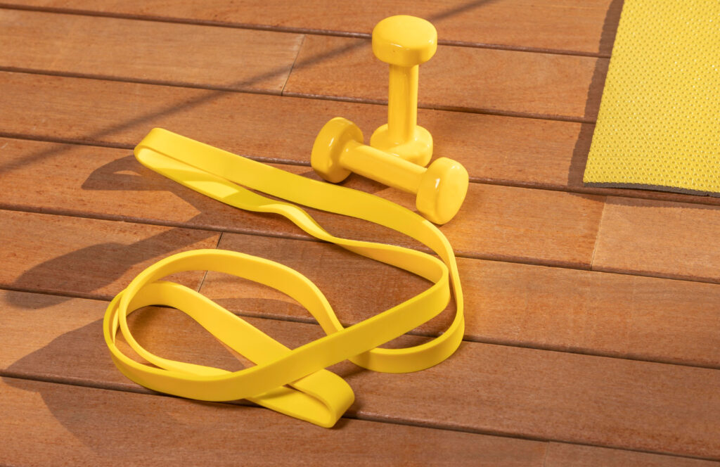 Des accessoires de fitness posés sur une surface ne bois: une élastique de couleur jaune, des mini haltères de couleur jaune et un tapis de couleur jaune.